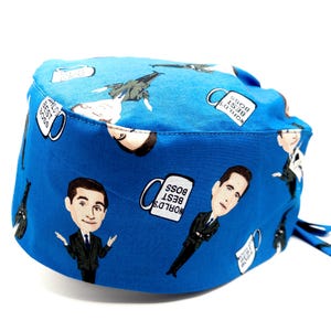 May include: Blue surgical scrub hat with a repeating pattern of a cartoon character holding a mug that says "World's Best Boss".