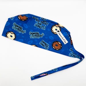 May include: Blue surgical scrub cap with a donut pattern. The cap has the text "General Surgery" and "Ask About Our Donuts!" printed on it.
