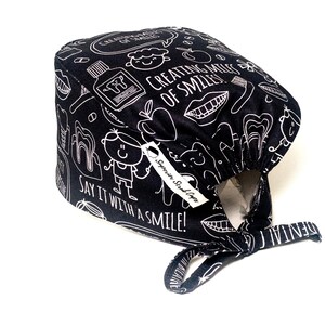 May include: Black scrub cap with a white print of dental-themed illustrations and the text "Creating Miles of Smiles" and "Say it with a smile!"