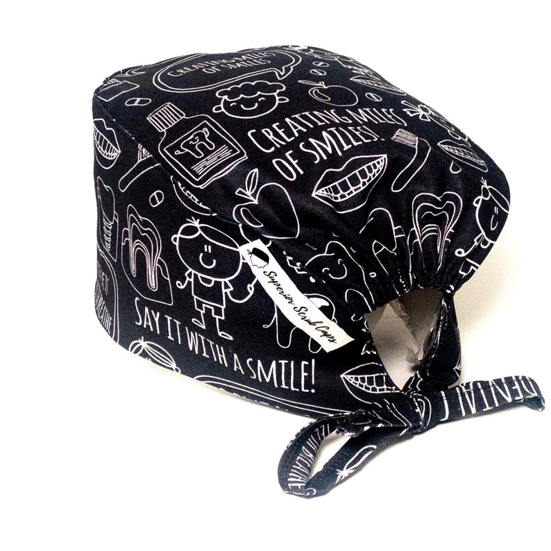 May include: Black scrub cap with a white print of dental-themed illustrations and the text "Creating Miles of Smiles" and "Say it with a smile!"