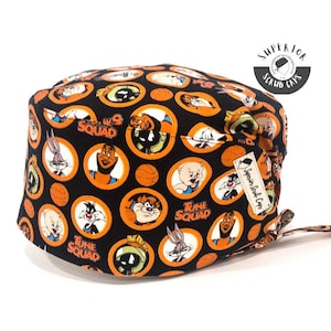 May include: Black scrub cap featuring cartoon characters in orange circles with basketballs. The cap has the words "Tune Squad" and "Superior Scrub Caps" on it. The cap is made of a soft, comfortable material.
