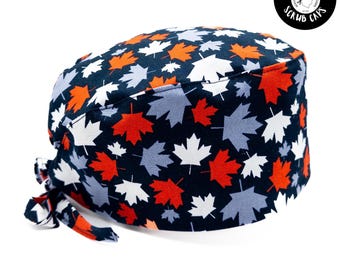 Pode incluir: Um gorro cirúrgico azul com um padrão de folhas de bordo brancas, vermelhas e cinzas. O gorro tem um laço na parte de trás.