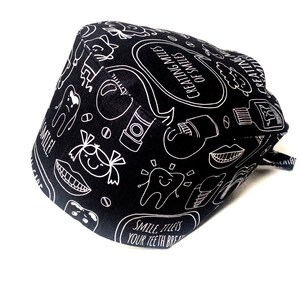 May include: Black scrub hat with a white design of dental-related illustrations and the text "Creating Miles of Smiles".