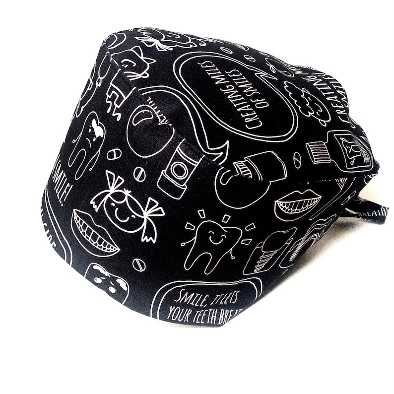 May include: Black scrub hat with a white design of dental-related illustrations and the text "Creating Miles of Smiles".