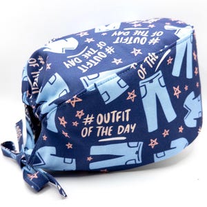 May include: Blue scrub hat with a white and pink print of jeans and stars. The text "#OUTFIT OF THE DAY" is repeated on the hat.