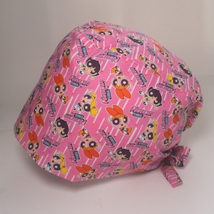 Könnte beinhalten: Rosaer chirurgischer Scrubb-Hut mit einem sich wiederholenden Muster der Powerpuff Girls-Charaktere und den Worten "Powerpuff Girls".