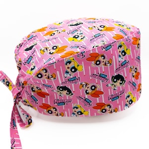 Könnte beinhalten: Rosa chirurgischer Scrubb-Hut mit einem sich wiederholenden Muster der Powerpuff Girls-Charaktere und den Worten "Powerpuff Girls".