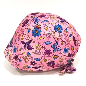 May include: Pink surgical scrub hat with a floral pattern featuring butterflies, flowers, and vines in shades of purple, blue, and yellow.