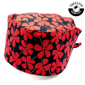Op de afbeelding: Een zwarte scrubcap met een rood bloemenpatroon. De cap heeft een afgeronde bovenkant en een brede rand. Het bloemenpatroon bestaat uit kleine rode bloemen op een zwarte achtergrond.