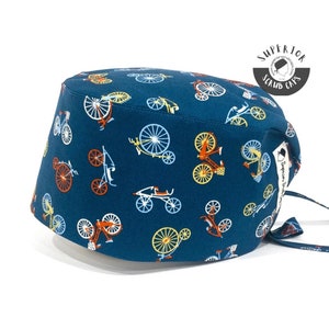 May include: A dark teal scrub cap featuring a repeating pattern of bicycles in shades of orange, yellow, and light blue. The cap includes a white fabric tag on the side with the text Superior Scrub Caps and a circular logo in the corner.