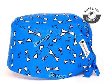 May include: A blue scrub cap with a pattern of white bones, hammers, and the word "ORTHO" in a playful font. The cap is made of a soft fabric and has a tie in the back for a secure fit. The cap is designed for medical professionals.