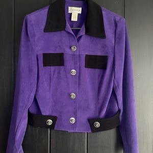 May include: A vibrant purple jacket featuring a contrasting black collar, two black chest pocket flaps, and a black hem band. The garment includes a front button closure with four silver-toned circular buttons and a Gantos brand label at the neck.