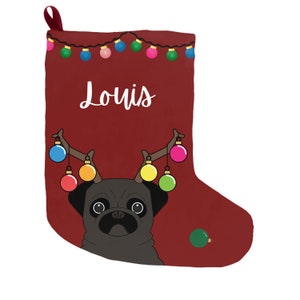 May include: A burgundy Christmas stocking featuring a black pug wearing antlers adorned with colorful ornaments. The name "Louis" is written in white script. A string of Christmas lights decorates the top, and a single ornament is on the side.