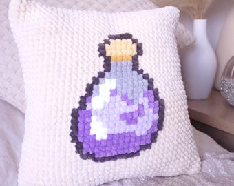 May include: A cream-colored square pillow with a pixelated purple potion bottle design. The bottle has a gray outline, a yellow top, and a light purple body. The pillow has a textured, plush surface.