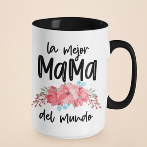 May include: White ceramic mug with a black rim and handle. The mug features black text that reads "la mejor Mama del mundo" with pink and blue watercolor flowers.