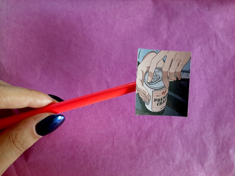 Może przedstawiać: Zbliżenie na rękę otwierającą puszkę napoju "PREMIUM CHAI". Puszka jest srebrna z czerwoną i białą etykietą. Ręka jest narysowana w stylu anime.