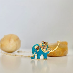 May include: A gold chain necklace with a turquoise enamel elephant pendant. The elephant has gold accents and clear rhinestones on its back.