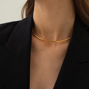 May include: A gold choker necklace with a simple, minimalist design. The necklace is made of a thin, smooth metal band.