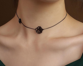 May include: A black choker necklace featuring a delicate rose design. The necklace has a thin chain and a small rose pendant near the clasp. The main focal point is a larger rose pendant centered on the neckline, creating an elegant accessory.