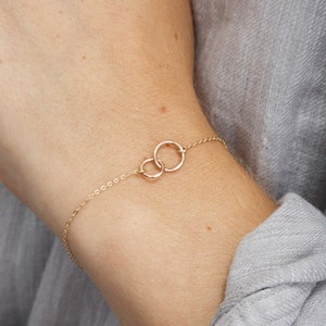 May include: A delicate gold chain bracelet with two interlocking circles. The bracelet is on a person's wrist.