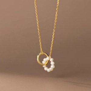 May include: A gold chain necklace with a delicate pendant featuring two interlocking circles, one adorned with small white pearls.
