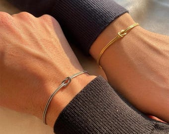 以下が含まれることがあります： 結び目のデザインが施されたシンプルなブレスレットが2つ。1つはシルバー、もう1つはゴールドです。