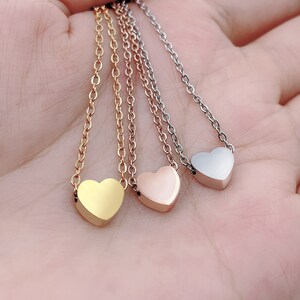 May include: Three delicate necklaces with small heart pendants. The necklaces are silver, gold, and rose gold.