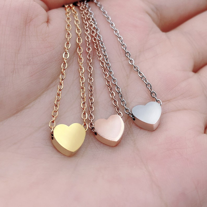 May include: Three delicate necklaces with small heart pendants. The necklaces are silver, gold, and rose gold.