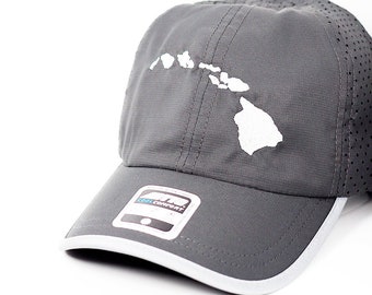 Può includere: Cappellino da baseball grigio con il contorno bianco delle isole Hawaii. Il cappellino ha una tesa bianca e un pannello laterale perforato. Un'etichetta con la scritta "Cool Comfort" è visibile sul davanti.