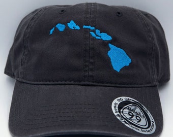 Può includere: Un cappellino da baseball grigio scuro con un contorno ricamato in blu chiaro delle isole hawaiane. Il cappellino ha una visiera curva e un piccolo adesivo circolare con testo.