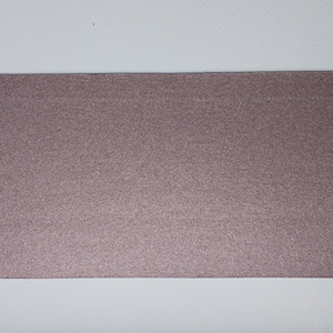 Könnte beinhalten: Ein rechteckiges Stück mauvefarbenes Papier mit einer glitzernden, strukturierten Oberfläche. Das Papier ist vor einem weißen Hintergrund platziert, wodurch ein Kontrast entsteht, der die Farbe und Textur des Papiers hervorhebt.