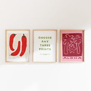 May include: Three framed art prints. The left print features red chili peppers on a beige background. The center print has green text that reads "CHOOSE ANY THREE PRINTS". The right print displays a red palm tree design with the word "ALOHA".