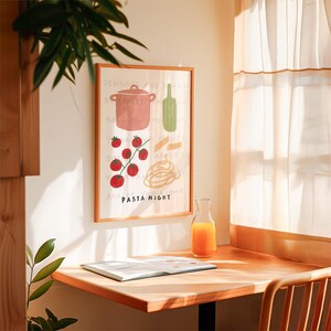 May include: A framed illustration of a pot, tomatoes, pasta, and a bottle of wine with the text "PASTA NIGHT" on a white background. The frame is brown wood and the illustration is in a minimalist style.