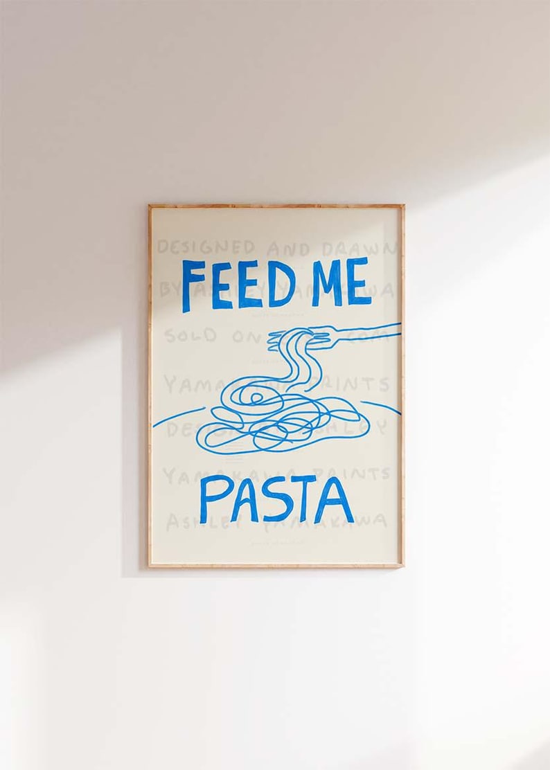 以下が含まれることがあります： 青い文字で「Feed Me Pasta」と書かれた、青と白の額装されたプリント。プリントには、フォークとスパゲッティの青い線画が描かれている。