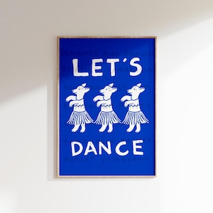 May include: A framed art print with a vibrant blue background. The print features three white dog-like figures in skirts, with the words "LET'S DANCE" in white block letters. The artwork is designed by Ashley Yamakawa.