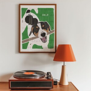 May include: A framed illustration of a dog named Arlo with a stick in its mouth. The dog is white with black and brown markings. The background is green.