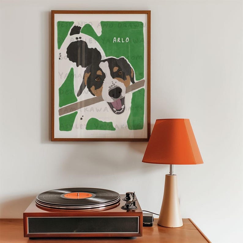 May include: A framed illustration of a dog named Arlo with a stick in its mouth. The dog is white with black and brown markings. The background is green.