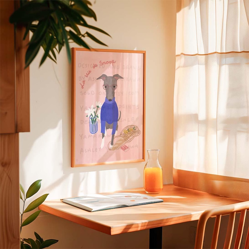 May include: A framed illustration of a grey dog wearing a blue jumper and glasses. The dog is standing on a pink background with text and a basket of flowers. The frame is brown wood.