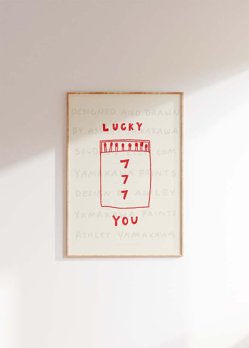 Peut inclure: Une impression encadr&eacute;e avec une illustration rouge d'une bo&icirc;te d'allumettes avec le mot "LUCKY" au-dessus et le nombre "7" r&eacute;p&eacute;t&eacute; quatre fois &agrave; l'int&eacute;rieur de la bo&icirc;te d'allumettes. Le texte "DESIGNED AND DRAWN BY ASHLEY YAMAKAWA" est au-dessus de la bo&icirc;te d'allumettes et le texte "YOU" est en dessous de la bo&icirc;te d'allumettes. Le texte "YAMAKAWA PRINTS" est en dessous du mot "YOU".