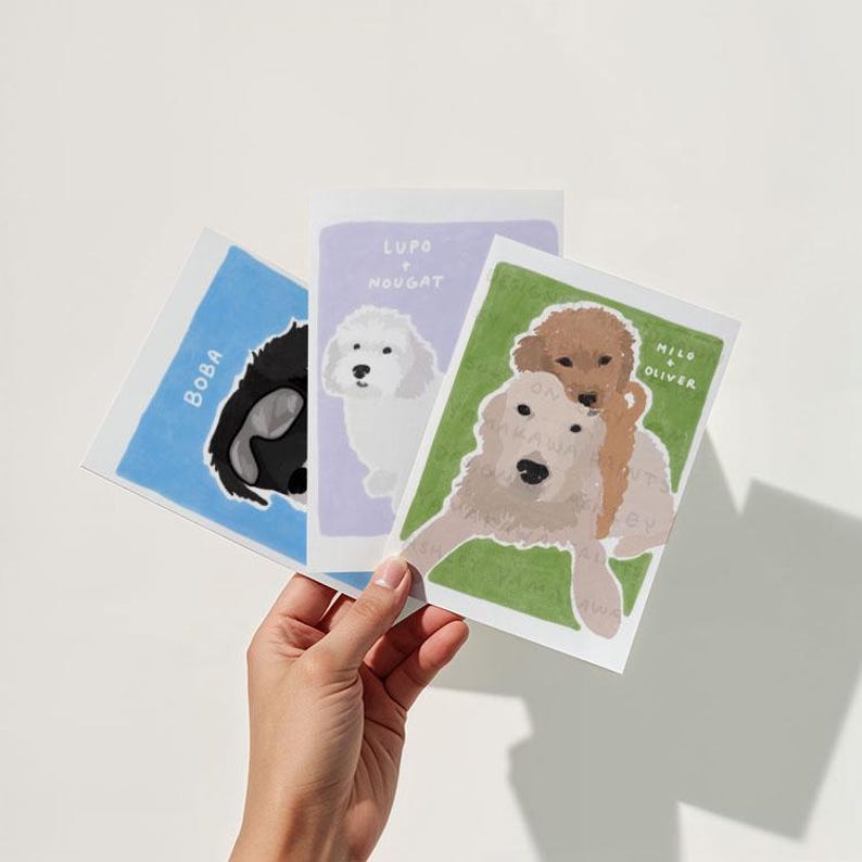 May include: Three illustrated cards featuring different dog breeds. The first card is blue with the name "Boba" written vertically. The second card is lavender with the names "Lupo & Nougat" written vertically. The third card is green with the names "Milo & Oliver" written vertically.