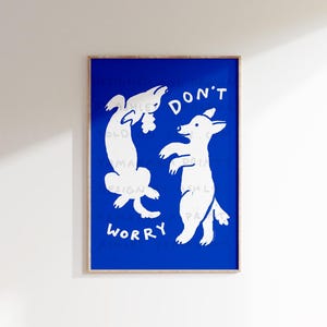 Puede incluir: Impresión artística enmarcada con un fondo azul, con dos ilustraciones de perros blancos y las palabras "DON'T WORRY". Los perros están representados en poses juguetonas. La obra de arte tiene un estilo minimalista y una estética moderna.