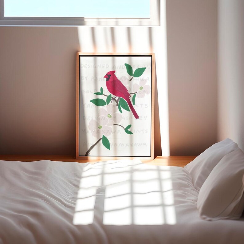 May include: A framed print of a red cardinal perched on a branch with white flowers. The print has a white background with text that reads "Designed and printed by Ashley Yamakawa".