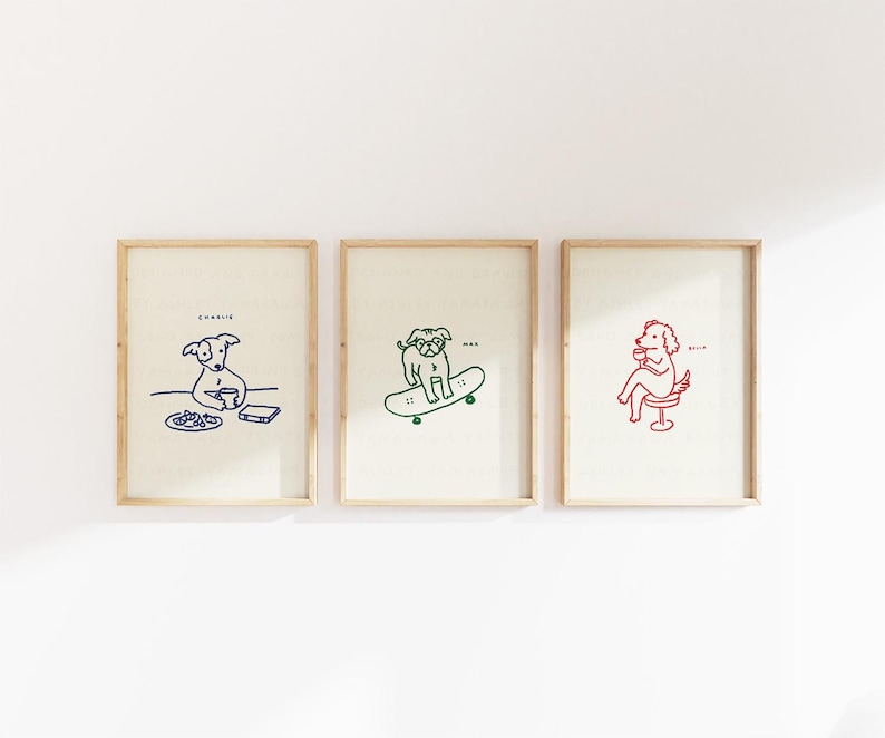 May include: Three framed art prints featuring line drawings of dogs. One print shows a blue dog at a table, another a green dog on a skateboard, and the third a red dog in a chair. Each print has a dog's name.