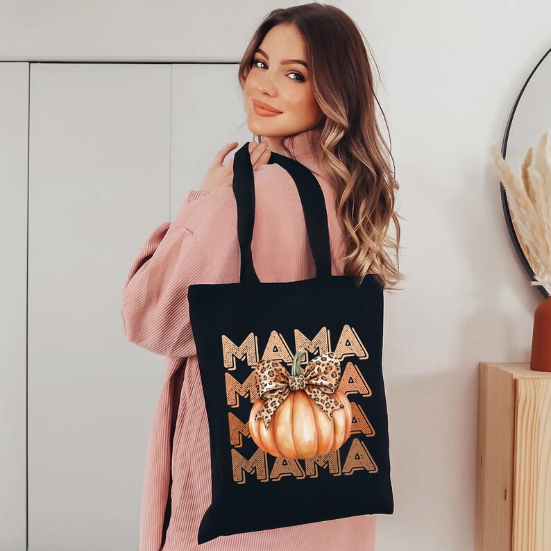 May include: Black tote bag with a graphic of a pumpkin with a leopard print bow and the word "MAMA" repeated in a gradient pattern.
