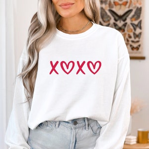 May include: White long-sleeve sweatshirt with a red "XOXO" graphic featuring hearts.