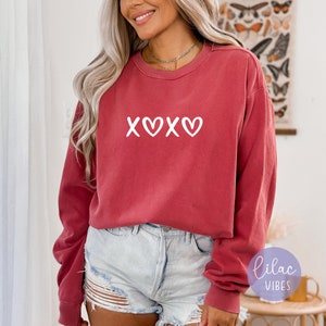 May include: A red long-sleeved sweatshirt with a white graphic that says "XOXO" with a heart in between the Os.