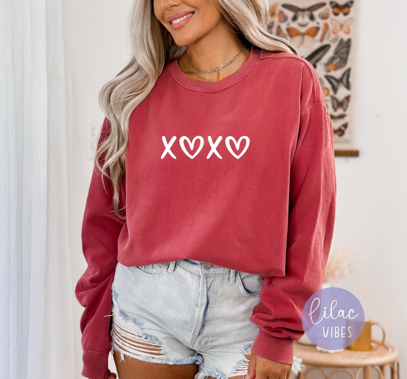May include: A red long-sleeved sweatshirt with a white graphic that says "XOXO" with a heart in between the Os.