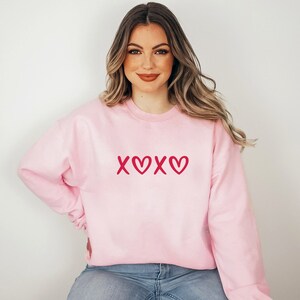 May include: A pink sweatshirt with a red "XOXO" graphic on the front.