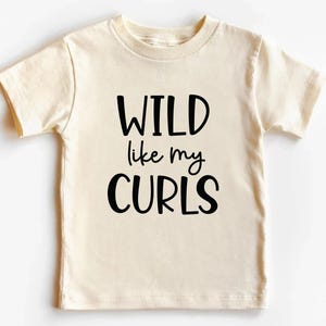 May include: A cream colored short-sleeved t-shirt with black text that reads "WILD like my CURLS".