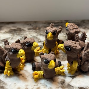May include: A group of small, brown and yellow bird figurines. The figurines have detailed wings and feet, with yellow beaks and feet. The birds are arranged together, with some standing and others lying down.